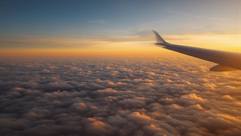 Asa de avião sobre nuvens douradas ao pôr do sol