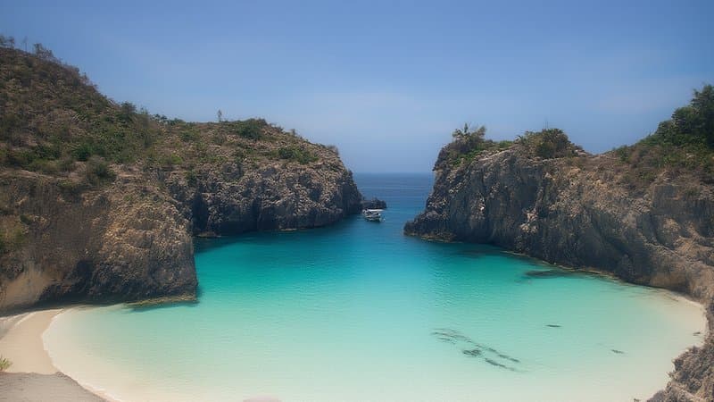 Enseada de água turquesa cristalina entre falésias em Arraial do Cabo com barco ao fundo