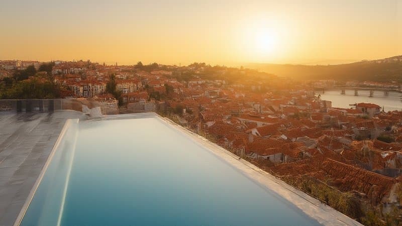 Terraço de hotel em Lisboa com piscina de borda infinita ao entardecer, com vista dos telhados da cidade e do rio Tejo